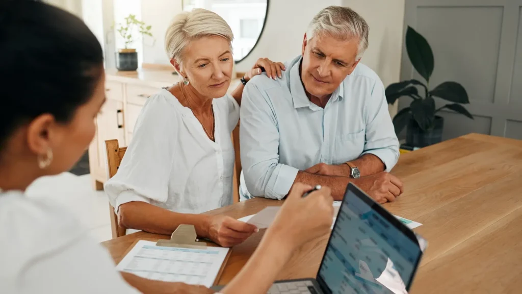 Senior couple meeting with a financial advisor at a table, reviewing documents and a laptop together